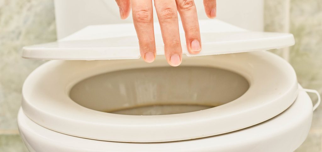 One hand is holding the lid of the commode and the calcium ring can be seen on the commode