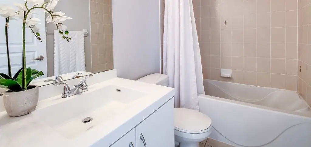The bathroom with tiles has a bathtub behind the white curtains and there are also toilet seats, bunnies, flowers tob.