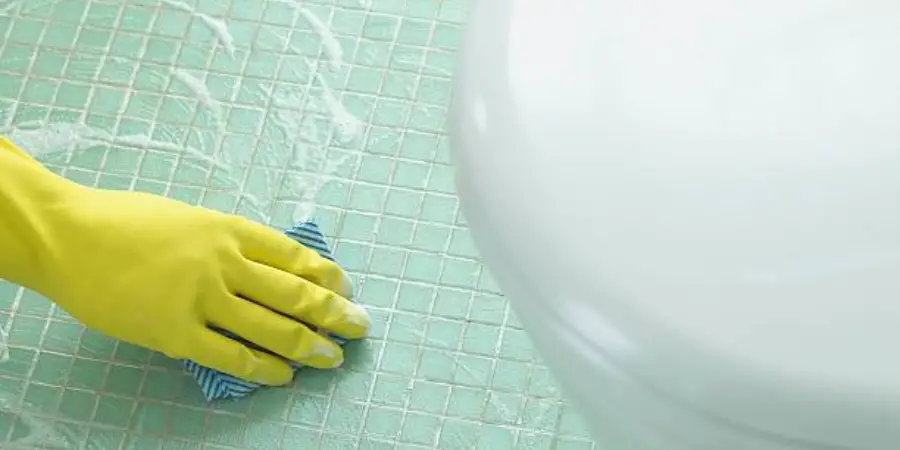 Cleaning the floor of the toilet by scrubbing with yellow gloves